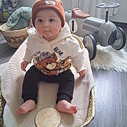 Noé participe au concours pour gagner de l'argent avec cette photo : baby, beanie, hoodie, bear_print, basket, blanket, toy_car, plush_bunny, flooring, indoors, child, cute, smiling, sitting, footwearless, wooden_floor, decor, soft_toys, number_one, warm_clothing