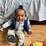 Kamari joined the competition — help win amazing prizes! toddler, child, indoor, floor, wooden_floor, shoe, black_shoes, hoodie, vest, hair_tied, curly_hair, expression, person, home, blanket, bed, casual_clothing, sitting, hand, playful