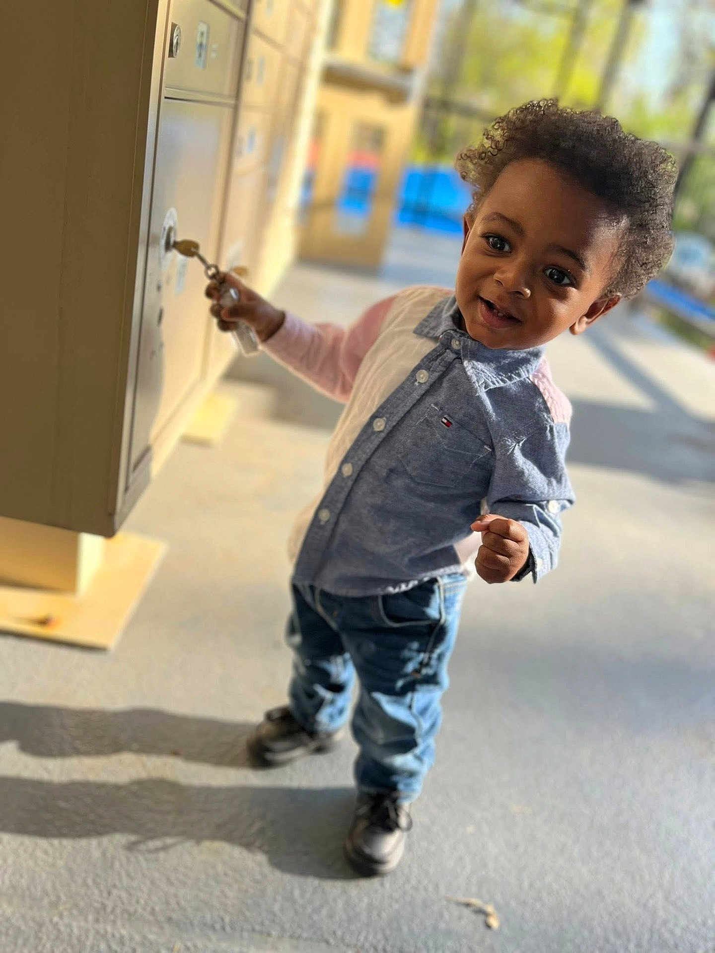 Kamari joined the competition — help win amazing prizes! child, toddler, boy, curly_hair, jeans, shirt, locker, key, holding, standing, outdoor, daylight, shadow, smiling, happy, casual_clothing, curious, portrait, person, young