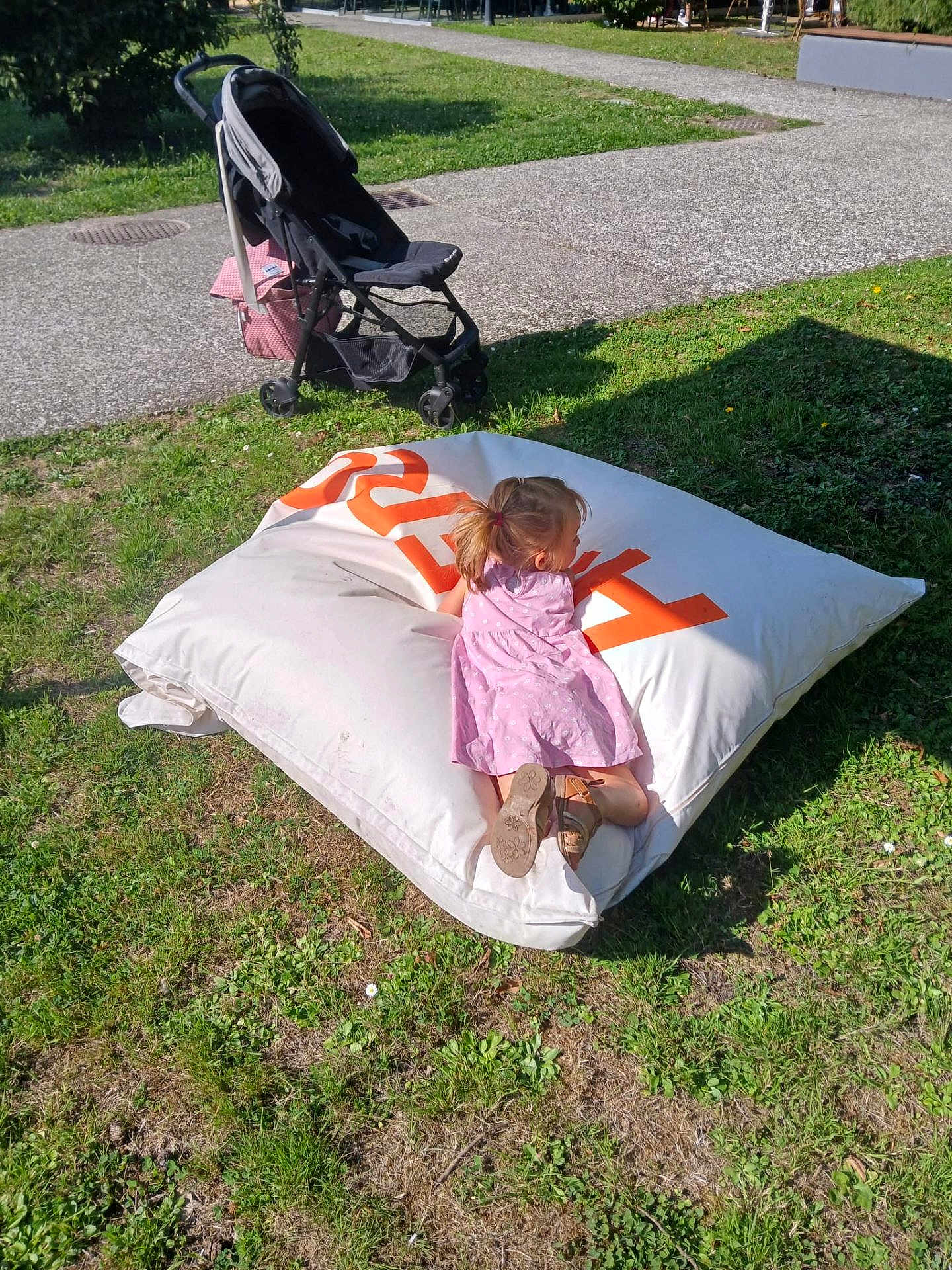 Ludmila participe au concours pour gagner de l'argent avec cette photo : child, girl, pink_dress, bean_bag, grass, outdoor, stroller, sunlight, shoes, pavement, park, play, relaxation, casual, daytime, greenery, summer, shadow, side_view, leisure