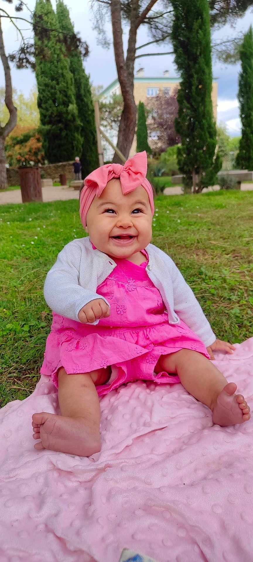 Arya a rejoint le concours — aidez-le/la à gagner de superbes lots ! baby, child, smiling, pink_dress, headband, bow, blanket, grass, outdoor, park, trees, happy, cute, infant, sitting, nature, daylight, person, feet, clothing