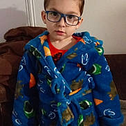 Diego a rejoint le concours — aidez-le/la à gagner de superbes lots ! child, boy, glasses, blue_robe, dinosaur_pattern, pajamas, portrait, indoor, living_room, couch, short_hair, looking_at_camera, face, hands, carpet, wall, cozy, standing, expressionless, kid