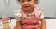 Karaji joined the competition — help win amazing prizes! baby, child, closeup, curly_hair, earring, foreground, gummy_smile, happy, indoor, infant, medical_room, photography, pink_overalls, portrait, sippy_cup, sitting, smiling, socks, striped_shirt, table