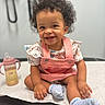 Karaji joined the competition — help win amazing prizes! baby, child, smiling, sitting, portrait, curly_hair, pink_overalls, striped_shirt, socks, sippy_cup, indoor, medical_room, table, happy, infant, gummy_smile, earring, foreground, closeup, photography