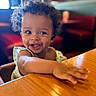 Karaji joined the competition — help win amazing prizes! baby, child, smiling, happy, curly_hair, portrait, indoor, restaurant, high_chair, wooden_table, reaching, arms, face, eyes, open_mouth, teeth, dress, seated, warm_lighting, candid_photography