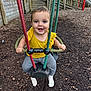 toddler, child, swing, playground, smiling, yellow_clothing, rope, wooden_fence, slide, outdoor, play, happy, park, seat, fun, daylight, person, feet, ground, woodchips
