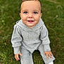 Ella is registered to the contest to win money with this photo: baby, child, smiling, outdoor, grass, greenery, knitwear, gray_clothing, cute, happy, sitting, face, portrait, young_child, innocence, bright_eyes, small_hands, cozy, casual, daylight