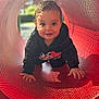 child, toddler, crawling, playground, red_tunnel, sunlight, shadow_pattern, happy, hoodie, outdoor, daylight, smile, face, curious, play, metal, perforated_surface, cute, young_child, fun