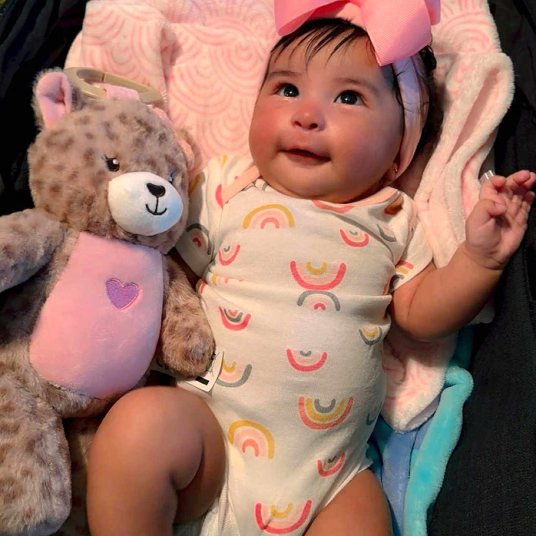 Ailany joined the competition — help win amazing prizes! baby, infant, child, portrait, smiling, bow, pink_bow, teddy_bear, stuffed_animal, blanket, onesie, rainbow_pattern, lying_down, indoors, cozy, happy, face, hands, feet, colorful