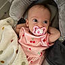 baby, pacifier, pink_clothing, cherry_pattern, blanket, polka_dot, infant, cushion, resting, wide_eyes, cute, portrait, indoor, comfortable, child, soft_texture, head_support, small_hands, curious, cozy