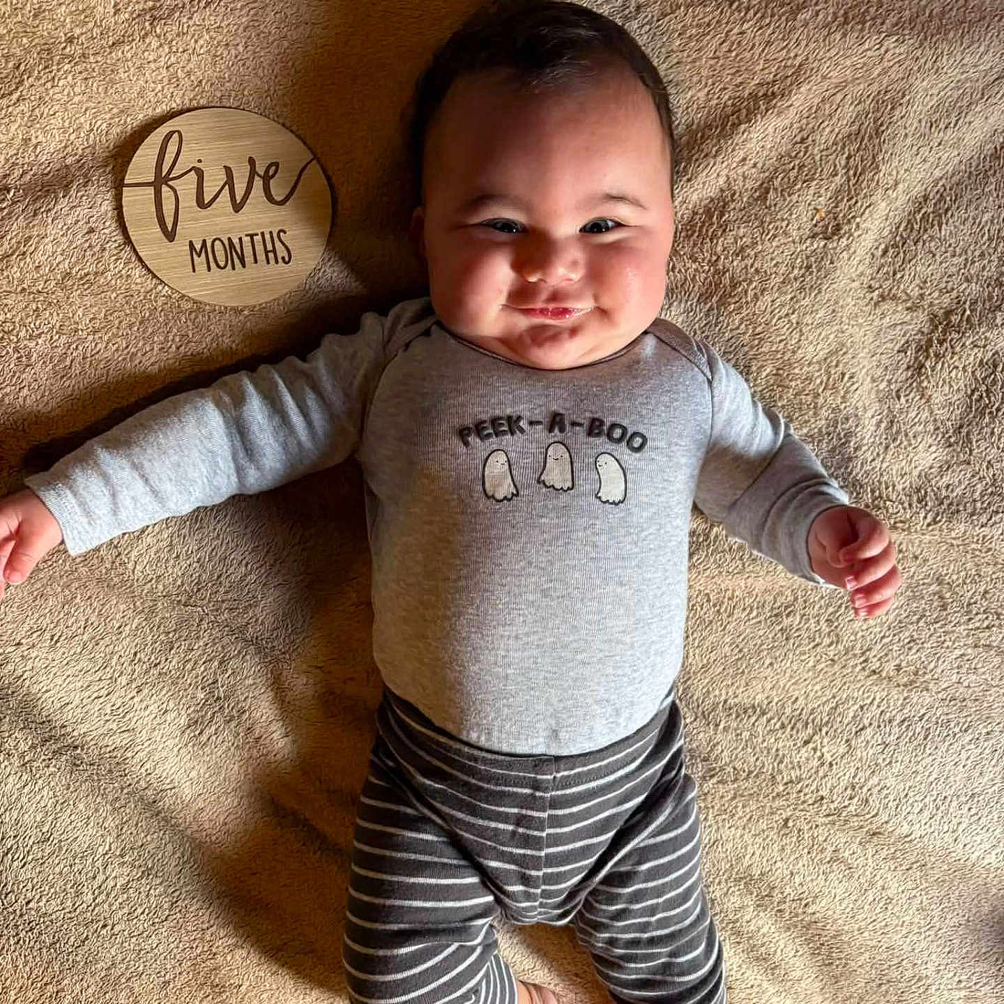 Koa joined the competition — help win amazing prizes! baby, infant, child, portrait, lying_down, smiling, face, five_months, blanket, indoors, gray_clothing, striped_pants, long_sleeves, bare_feet, wooden_sign, peekaboo, happy, playful, soft_lighting, cozy