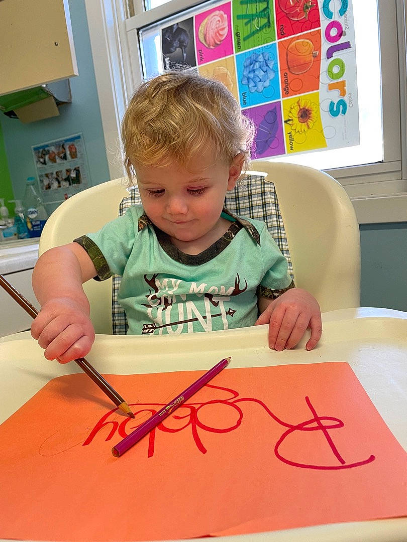 Robby is registered to the contest to win money with this photo: arm, art, chair, child, eyelash, finger, font, fun, illustration, paint, person, play, room, shirt, t_shirt, table, toddler, visual_arts, window, writing