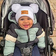 Ilyes a rejoint le concours — aidez-le/la à gagner de superbes lots ! baby, child, stroller, jacket, hat, pom_poms, smile, happy, outdoor, pavement, baby_clothing, winter_wear, cute, infant, person, seat_belt, footwear, cold_weather, baby_stroller, urban