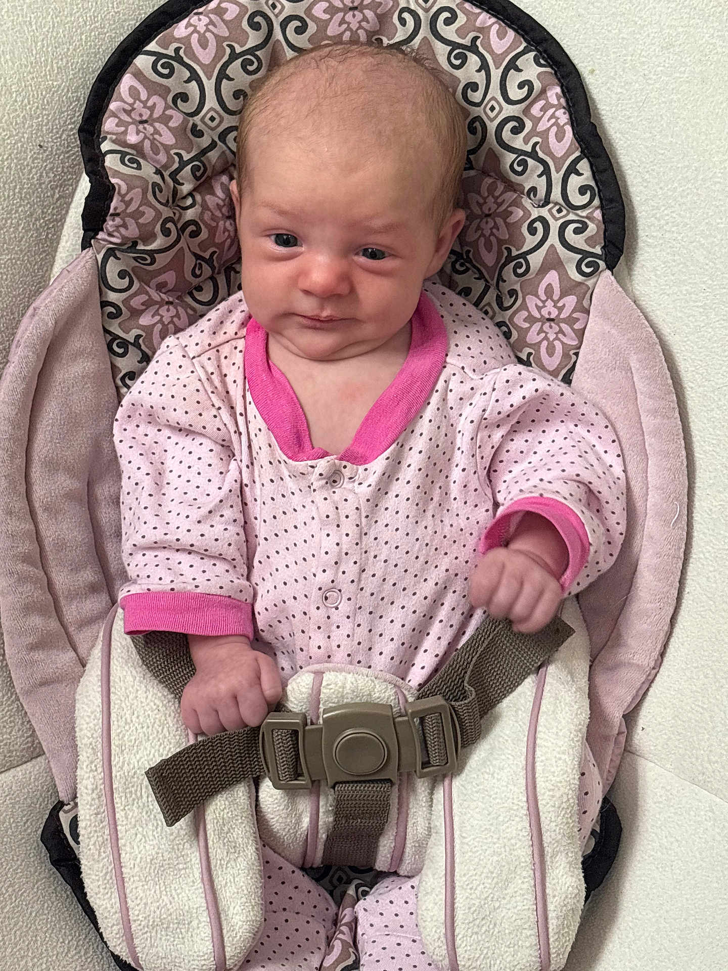 Evelynn is registered to the contest to win money with this photo: baby, infant, child, onesie, pink_clothing, polka_dot, baby_seat, cushion, safety_strap, indoor, person, face, hand, seat, fabric, pattern, cute, newborn, expression, small