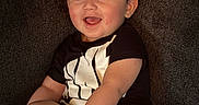 Tommy is registered to the contest to win money with this photo: baby, child, smiling, happy, sitting, couch, clothing, black_shirt, white_shoes, indoor, person, infant, cute, portrait, young_child, hands, feet, face, hair, comfort