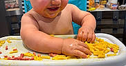 Nolan joined the competition — help win amazing prizes! baby, high_chair, macaroni_and_cheese, messy, food, kitchen, smiling, child, face, hands, tray, foot, expression, indoor, furniture, person, happy, meal, cute, eating