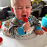 Nolan is registered to the contest to win money with this photo: baby, crying, lollipop, pajamas, infant, child, tears, indoor, toy, walker, face, expression, person, furniture, living_room, comfort, emotion, hand, clothing, home