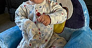 Nolan is registered to the contest to win money with this photo: baby, carpet, child, colorful, cute, expression, face, furniture, hand, home, indoor, lollipop, pajamas, person, plush_chair, room, sitting, star_pattern, toddler, toy