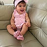 baby, child, smiling, pink_clothing, headband, bow, sitting, leather_couch, indoor, cute, happy, shoes, footwear, bracelet, infant, person, portrait, young_child, fashion, home