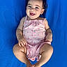 baby, child, smiling, happy, cute, infant, romper, pink, blue_background, bow, hair_accessory, lying_down, barefoot, skin, portrait, one_person, indoors, toddler, bracelet, playful