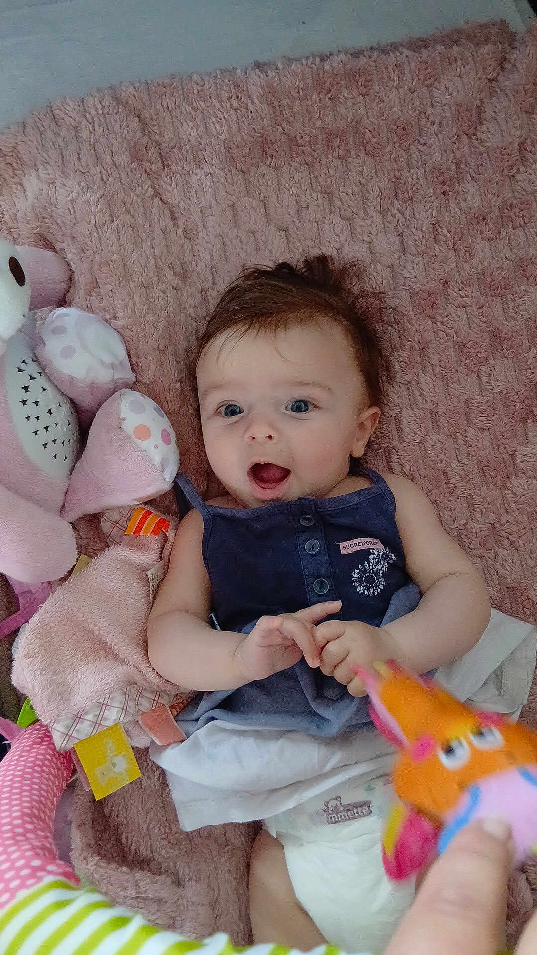 Eléna participe au concours pour gagner de l'argent avec cette photo : baby, infant, blanket, plush_toy, diaper, clothing, hand, person, soft_toy, blue_eyes, smiling, lying_down, fabric, pink, texture, toy, cute, child, indoor, play