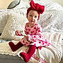 toddler, child, girl, heart_pattern, dress, red_tights, red_bow, headband, giraffe_toy, sofa, pillows, blanket, indoor, cute, smiling, portrait, cozy, comfort, baby, seated