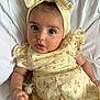 Meliha is registered to the contest to win money with this photo: baby, infant, child, yellow_dress, headband, pacifier, cute, portrait, indoors, soft_lighting, close_up, hand, face, eyes, skin, expression, fabric, bed, blanket, sleepwear