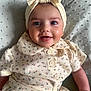 Meliha is registered to the contest to win money with this photo: baby, smile, face, headband, clothing, floral_pattern, buttoned_shirt, blanket, infant, portrait, cute, happy, child, skin, hand, texture, lying_down, indoors, soft_light, closeup