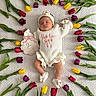 baby, infant, sleeping, tulips, flowers, blanket, white_clothing, headband, sign, month_marker, colorful, nature, floral_arrangement, cute, newborn, soft_texture, peaceful, indoors, baby_accessories, portrait