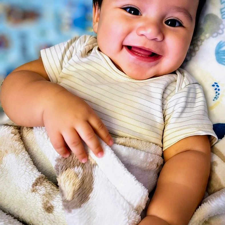 Bryson is registered to the contest to win money with this photo: baby, smiling, blanket, cozy, cute, infant, happy, child, portrait, face, hand, soft, fabric, indoors, young, person, clothing, striped_shirt, skin, closeup