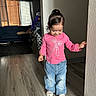 toddler, child, indoor, pink_shirt, blue_jeans, white_shoes, wooden_floor, living_room, couch, curtains, window, wall, smiling, hair_tied, person, clothing, home, flooring, balance, cute