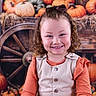 autumn, beige_vest, child, curly_hair, cute, decoration, fall, festive, happy, harvest, holiday, orange_shirt, outdoor_theme, portrait, pumpkins, rustic, seasonal, smiling, wagon_wheel, wooden_background