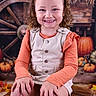 autumn, background, beige_dress, boots, child, curly_hair, cute, decor, fall, festive, happy, indoor, orange_shirt, portrait, pumpkins, rustic, seasonal, smiling, wagon_wheel, wooden_chest