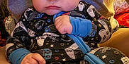 Brady is registered to the contest to win money with this photo: baby, infant, child, person, onesie, pajamas, video_game_controller, pattern, hands, face, portrait, sitting, couch, adult_torso, nike_shirt, zipper, eyes, cute, indoor, soft_lighting