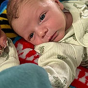 Brady joined the competition — help win amazing prizes! baby, infant, newborn, face, blue_eyes, blanket, onesie, clothing, cozy, close_up, portrait, lying_down, soft_texture, tiny_hand, adult_hand, nail_art, dinosaur_print, red_blanket, pattern, sleepy