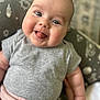 baby, child, tongue_out, blue_eyes, chubby_cheeks, grey_shirt, pink_pants, cushion, patterned_background, indoor, smiling, cute, infant, portrait, seated, happy, plush, closeup, person, soft_lighting