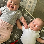 Eleanor joined the competition — help win amazing prizes! baby, infant, two_babies, smiling, lying_down, cushion, space_pattern, holding_hands, cute, indoors, clothing, onesie, pink_pants, gray_shirt, white_shirt, black_pants, red_toy, face, portrait, happy
