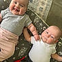 baby, infant, two_babies, smiling, lying_down, cushion, space_pattern, holding_hands, cute, indoors, clothing, onesie, pink_pants, gray_shirt, white_shirt, black_pants, red_toy, face, portrait, happy