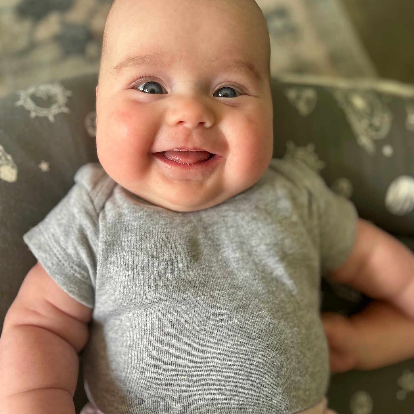 Eleanor is registered to the contest to win money with this photo: arm, baby, celestial_designs, child, chubby_cheeks, close_up, cushion, cute, eyes, face, gray_shirt, happy, indoor, infant, patterned, person, pink_pants, plump, portrait, smiling