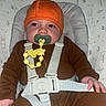 baby, child, infant, portrait, sitting, pacifier, hat, orange_hat, pumpkin_hat, brown_clothing, harness, safety_straps, baby_seat, cushion, bunny_pattern, woodland_theme, indoor, close_up, face, calm