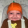 baby, child, infant, portrait, close_up, face, smiling, rosy_cheeks, orange_hat, knit_hat, brown_clothing, straps, baby_seat, yellow_toy, pacifier_clip, indoor, seated, looking_at_camera, soft_background, safe