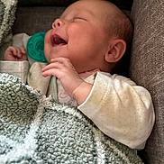 Amaya is registered to the contest to win money with this photo: baby, infant, blanket, smile, laughing, pacifier, couch, soft_furniture, cozy, sleepwear, child, happy, relaxed, indoor, portrait, cute, hand, head, face, newborn