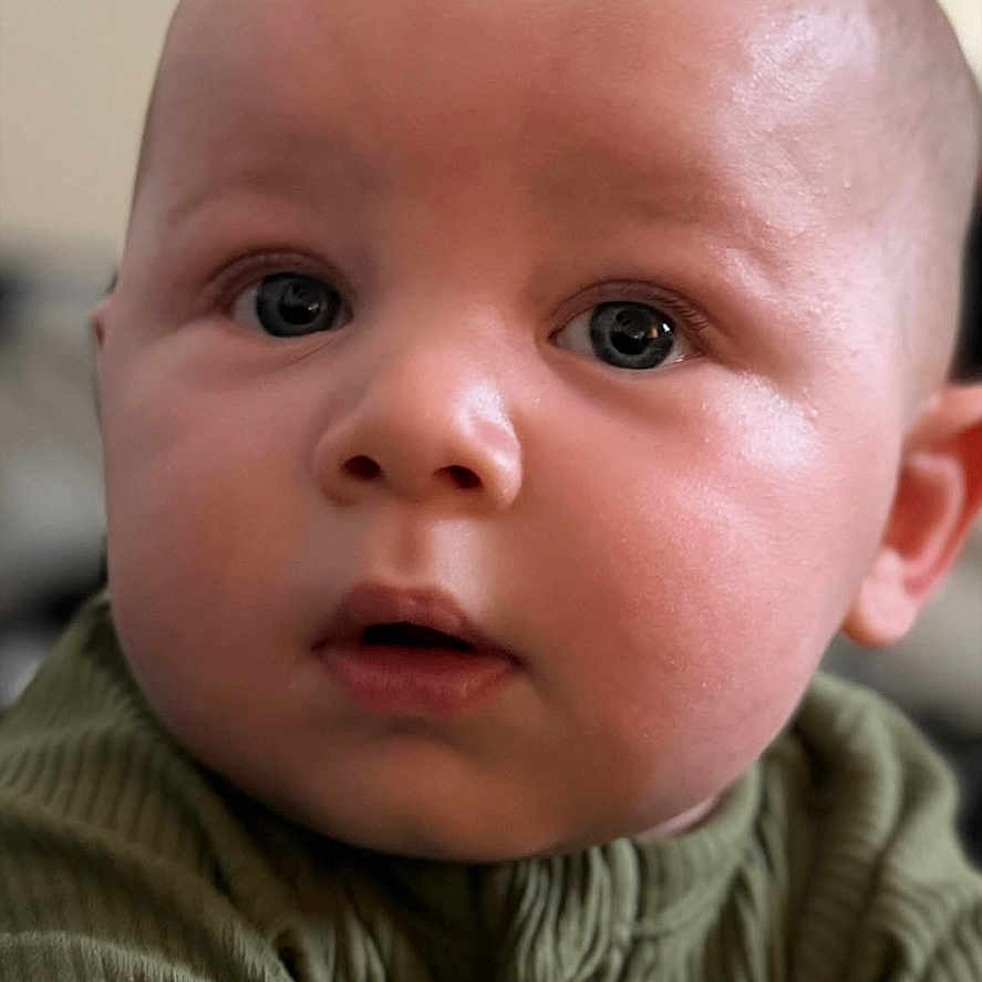 Kash joined the competition — help win amazing prizes! baby, infant, face, closeup, indoor, portrait, child, green_clothing, curious, expression, young, skin, eyes, head, cute, soft_light, background_blur, human, person, text_overlay