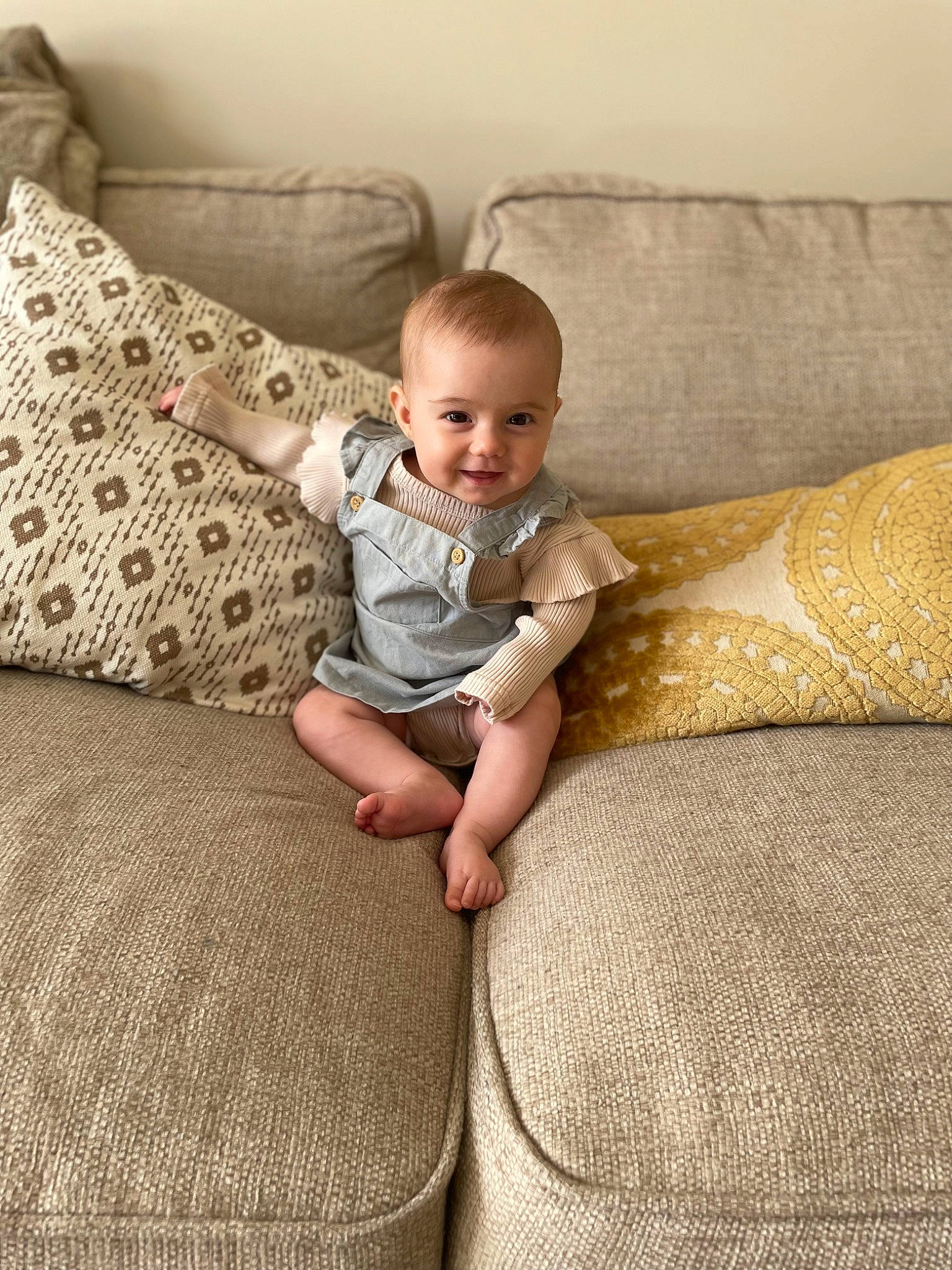 Aubrey is registered to the contest to win money with this photo: baby, baby_toddler_clothing, child, comfort, couch, eye, floor, flooring, hardwood, human_leg, joy, linens, living_room, person, sitting, skin, smile, studio_couch, textile, throw_pillow