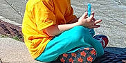 Sacha participe au concours pour gagner de l'argent avec cette photo : child, boy, glasses, orange_shirt, blue_pants, sitting, smiling, outdoor, pavement, sunny, bubble_wand, happy, casual_clothing, playful, daytime, young, person, footwear, urban, relaxed