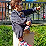 child, boy, pajamas, sneakers, glasses, pointing, grass, fence, outdoor, daylight, utility_box, building, sky, toy, expression, person, casual, nature, sunlight, playful