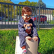 Sacha a rejoint le concours — aidez-le/la à gagner de superbes lots ! child, boy, glasses, outdoor, grass, toy, sneakers, fence, sunlight, smile, greenery, playful, casual_clothing, daylight, young, person, nature, happy, sitting, park