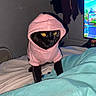 cat, black_cat, hoodie, pink_hoodie, pet_clothing, indoor, bed, blanket, yellow_eyes, feline, cute, animal, pet, domestic_cat, looking, animal_portrait, closeup, cozy, home, night