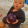 baby, child, indoor, carpet, toy, purple_ball, onesie, kneeling, curious, expression, person, floor, playroom, childrens_toy, home, infant, young_child, face, hands, candid
