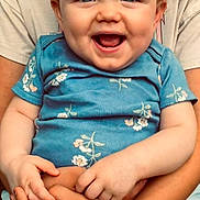Kleo joined the competition — help win amazing prizes! baby, smiling, child, blue_onesie, floral_pattern, hands, adult_hands, holding, happy, portrait, cute, infant, casual_clothing, denim_shorts, beige_shirt, indoor, closeup, person, skin, face